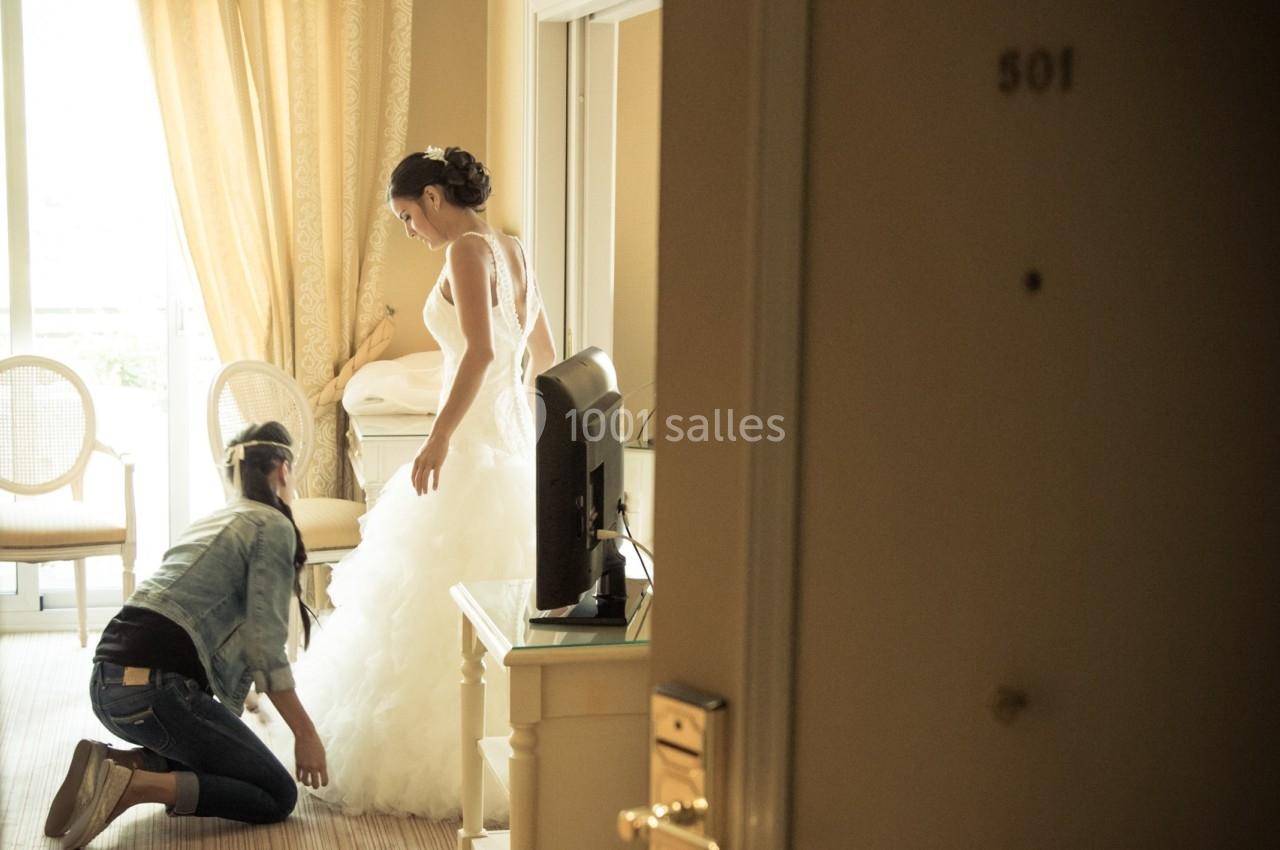 Location salle Divonne-les-Bains (Ain) - Domaine de Divonne #14 Une femme ajuste la robe de mariée d'une autre femme dans une chambre d'hôtel lumineuse.