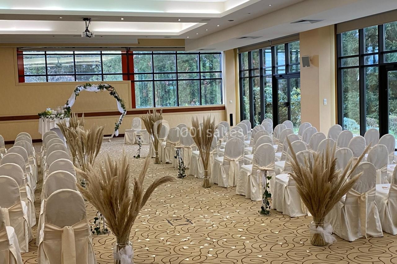 Location salle Divonne-les-Bains (Ain) - Domaine de Divonne #5 Salle de réception décorée pour une cérémonie, avec des rangées de chaises blanches et des ornements floraux.