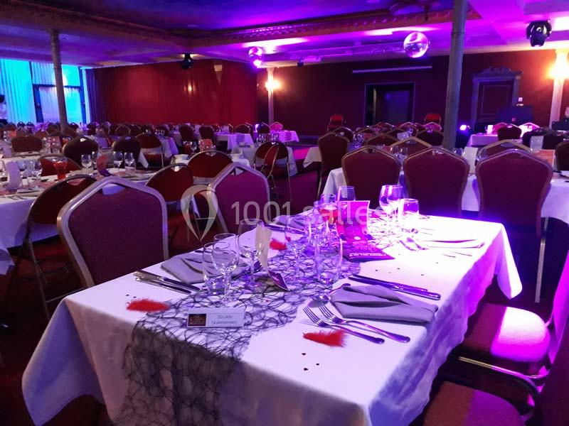 Salle de réception avec tables dressées, nappes blanches, verres, couverts et décorations lumineuses violettes.