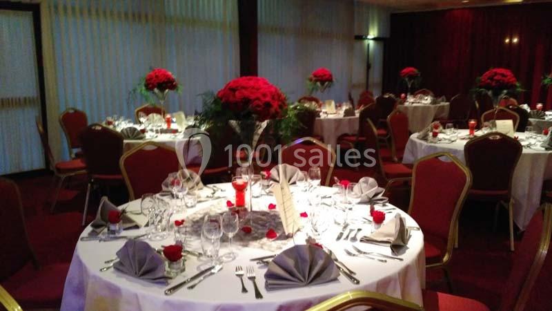 Salle de réception décorée pour un événement, avec tables rondes ornées de nappes blanches, serviettes pliées et bouquets de…