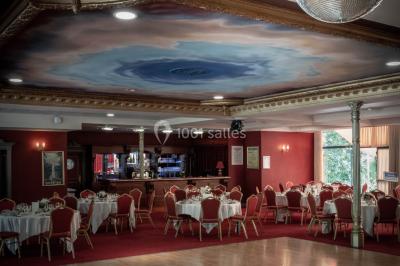 Salle de réception avec scène, piste de danse en bois, moquette rouge et plafond décoré d'une fresque.