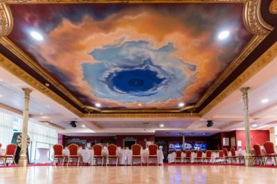 Salle de réception avec scène, piste de danse en bois, moquette rouge et plafond décoré d'une fresque.