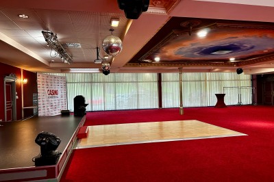 Salle de réception avec scène, piste de danse en bois, moquette rouge et plafond décoré d'une fresque.