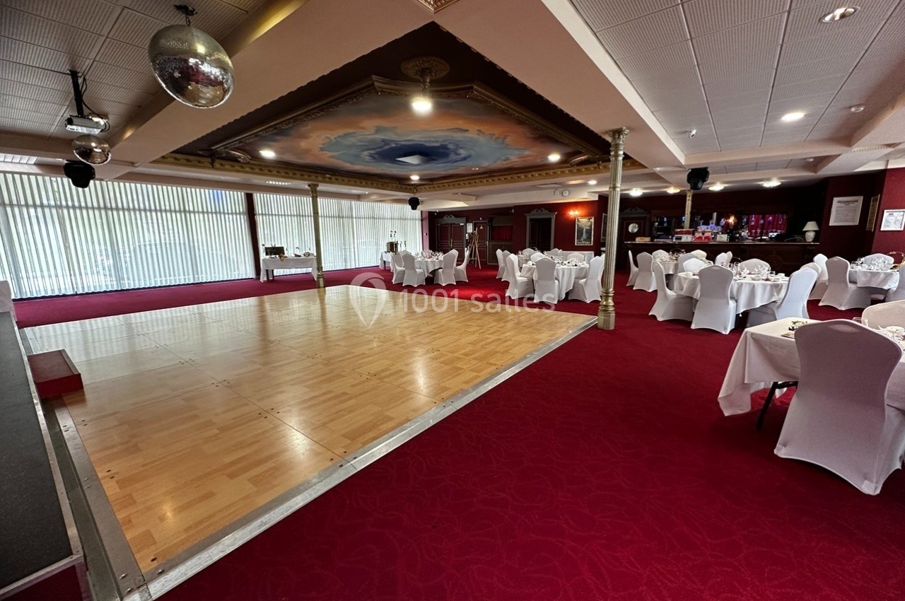 Salle de réception avec parquet pour danse, tables dressées avec nappes blanches et plafond décoré.