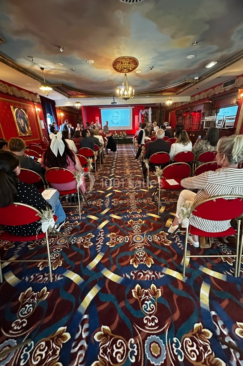 Avant la cérémonie Personnes assises dans une salle ornée de décorations rouges et dorées, assistant à une présentation sur écran.