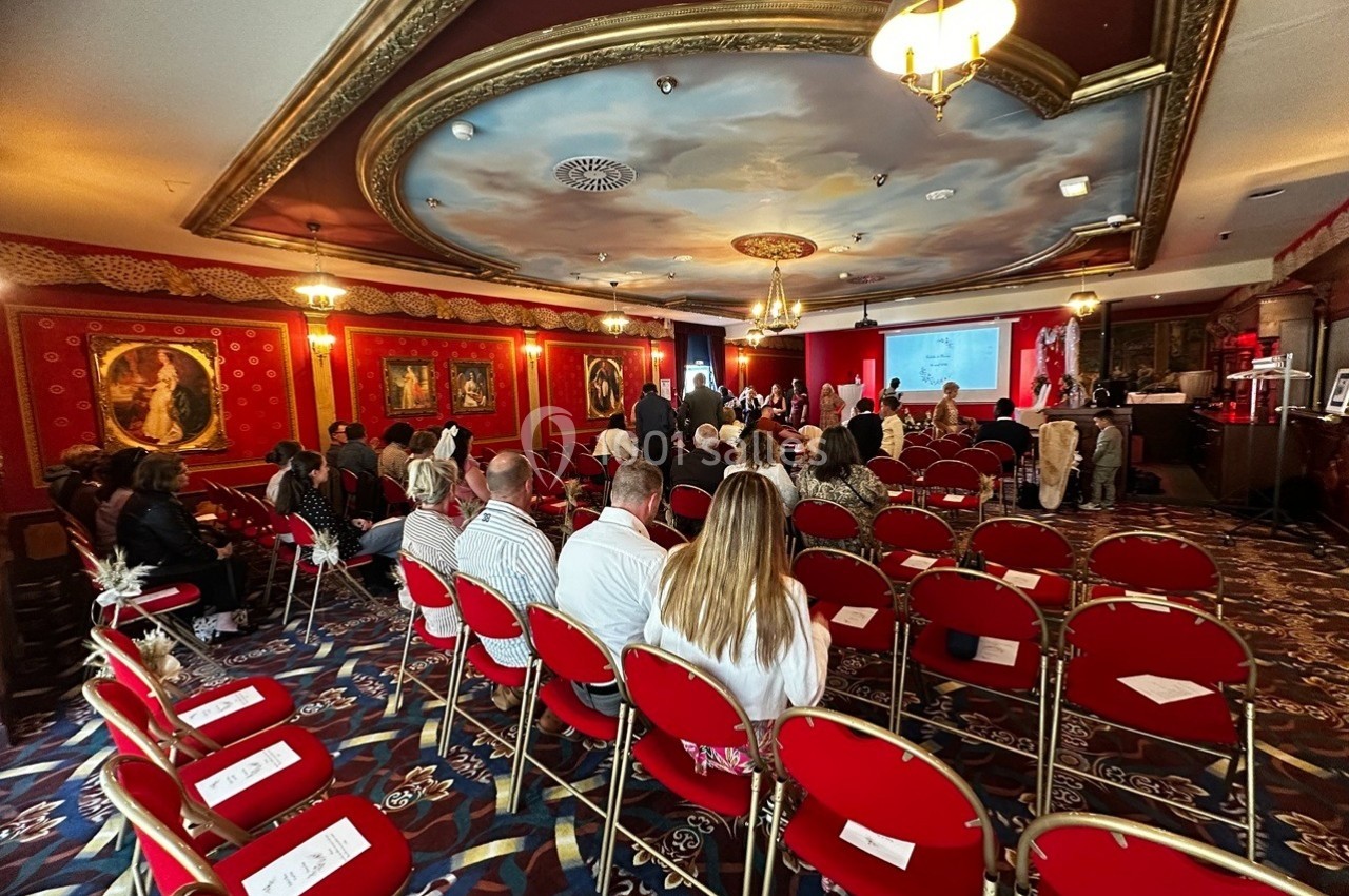 Salle de conférence avec des participants assis sur des chaises rouges, regardant une présentation projetée à l'écran.