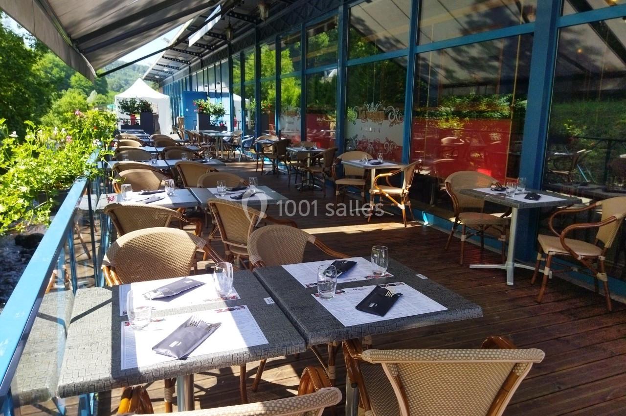 Terrasse en bois d'un restaurant avec des tables dressées, entourée de verdure et partiellement ombragée par des auvents.