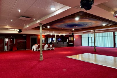 Salle de réception avec scène, piste de danse en bois, moquette rouge et plafond décoré d'une fresque.