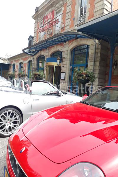 Deux voitures décapotables garées devant un bâtiment en briques avec une enseigne ’Casino Plombières’.