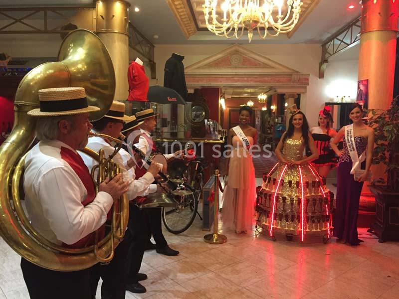 Un groupe de musiciens joue devant quatre femmes en robes élégantes dans un hall éclairé.
