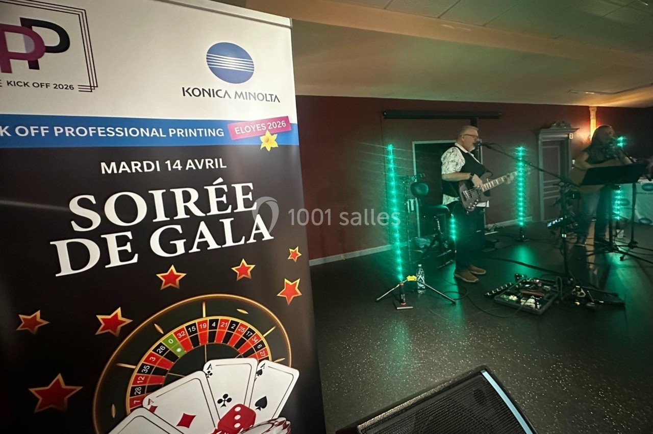 Animation sur scène Un musicien joue de la guitare sur scène lors d'une soirée de gala, avec une affiche promotionnelle au premier plan.