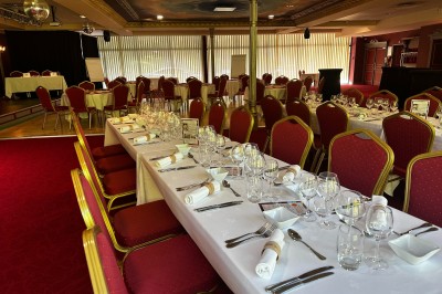 Miniature Après la plénière, repas dans le Salon Impérial Bâtiment en briques rouges avec horloge, entouré de verdure, situé près d'un ruisseau et d'une pente herbeuse.