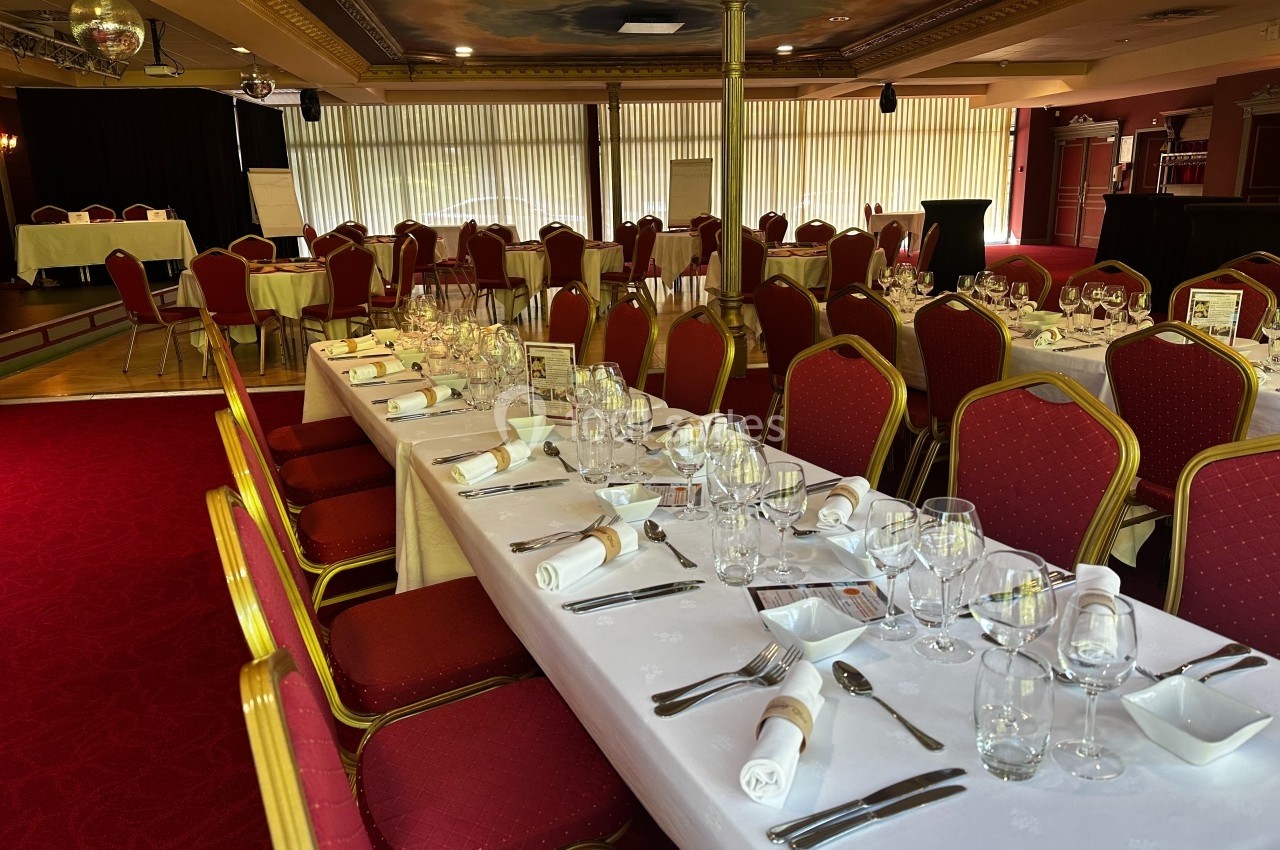 Après la plénière, repas dans le Salon Impérial Salle de réception avec tables dressées, nappes blanches, chaises rouges et lumière naturelle filtrée par des stores.