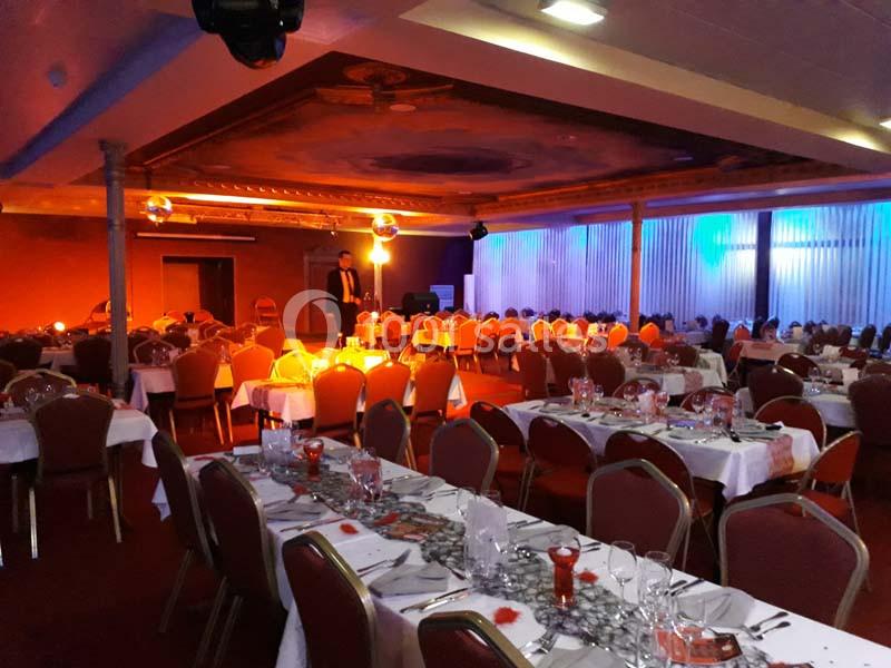 Salle de réception décorée avec des tables dressées pour un événement, éclairage chaleureux et ambiance festive.