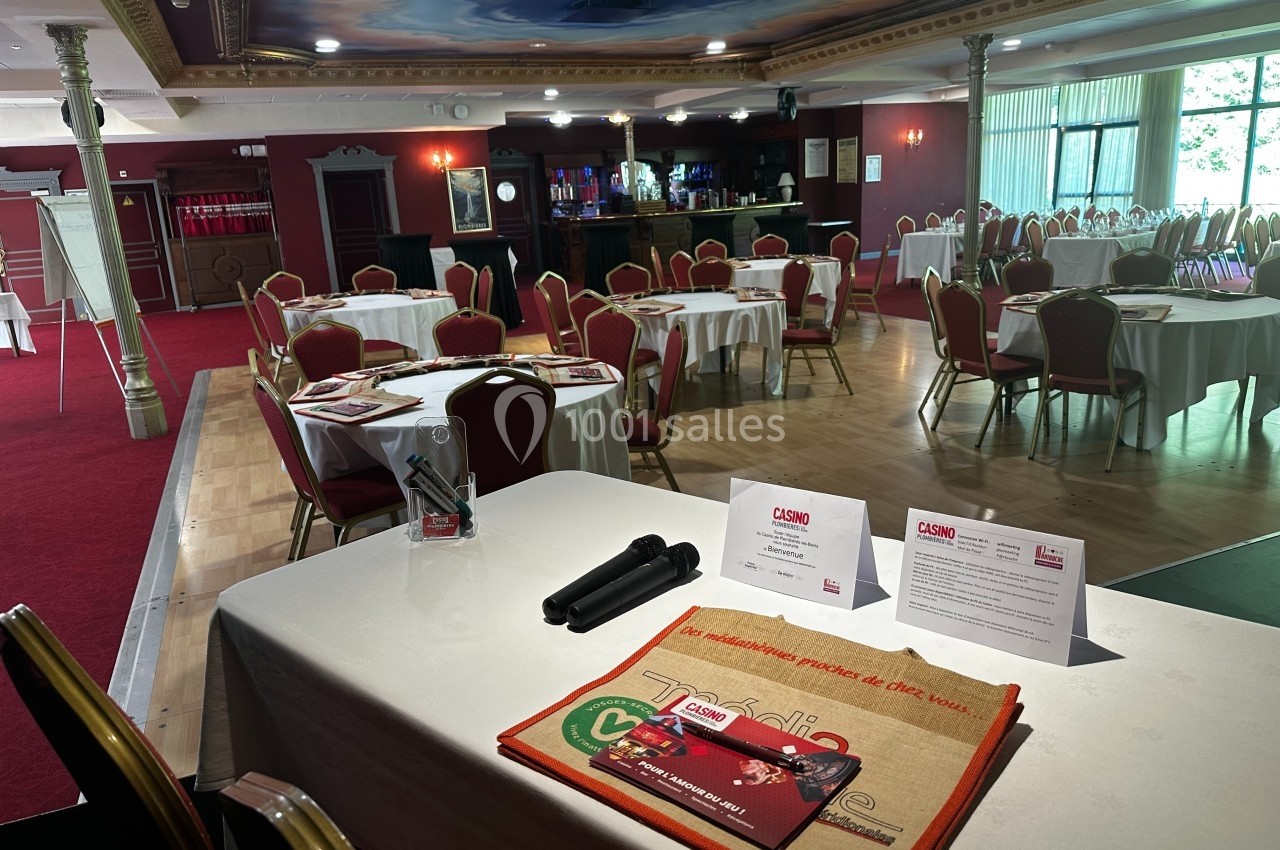 Avant l'arrivée des participants de la journée/séminaire Salle de conférence avec tables rondes dressées, documents promotionnels et micros sur une table au premier plan.