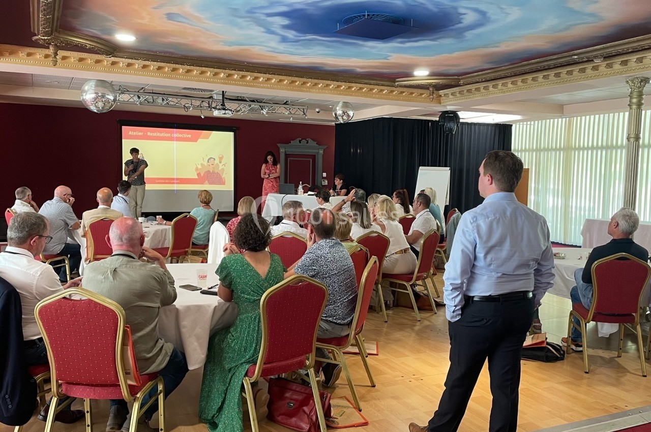 De bonnes conditions pour travailler et échanger Groupe de personnes assises dans une salle de conférence, écoutant une présentation projetée sur un écran.