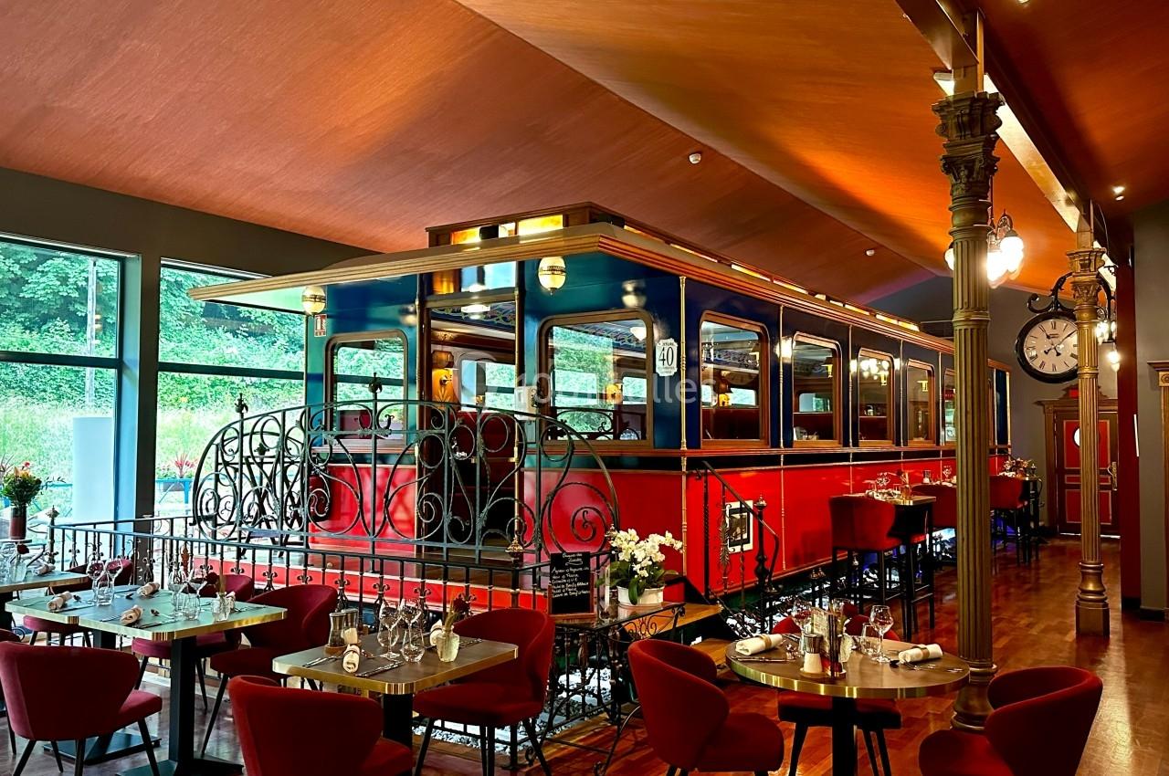 Wagon de train rouge aménagé en salle de restaurant, entouré de tables dressées dans un décor chaleureux.