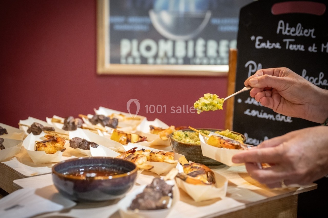 Gourmandise et découverte à l'atelier entre Assortiment de plats et amuse-bouches présentés sur une table, une main servant une préparation avec une cuillère.