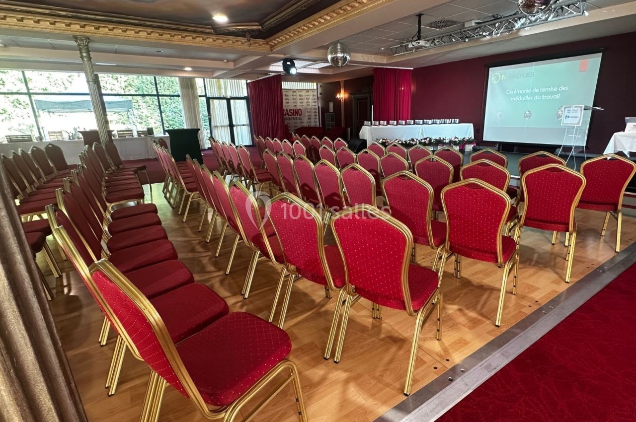 Idéal pour remise de prix Salle de conférence avec des rangées de chaises rouges alignées face à un écran de projection et une scène.