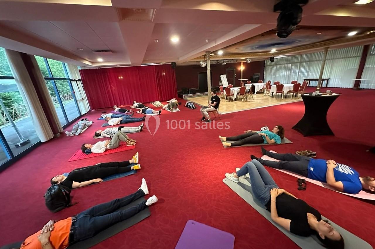 Personnes allongées sur des tapis dans une salle avec moquette rouge, participant à une séance de relaxation ou de…