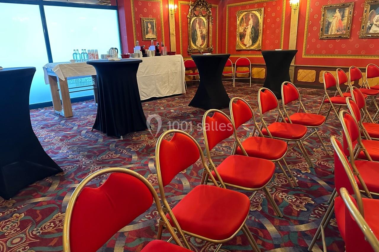 Salle de réception avec chaises rouges alignées, tables hautes noires et buffet en arrière-plan.