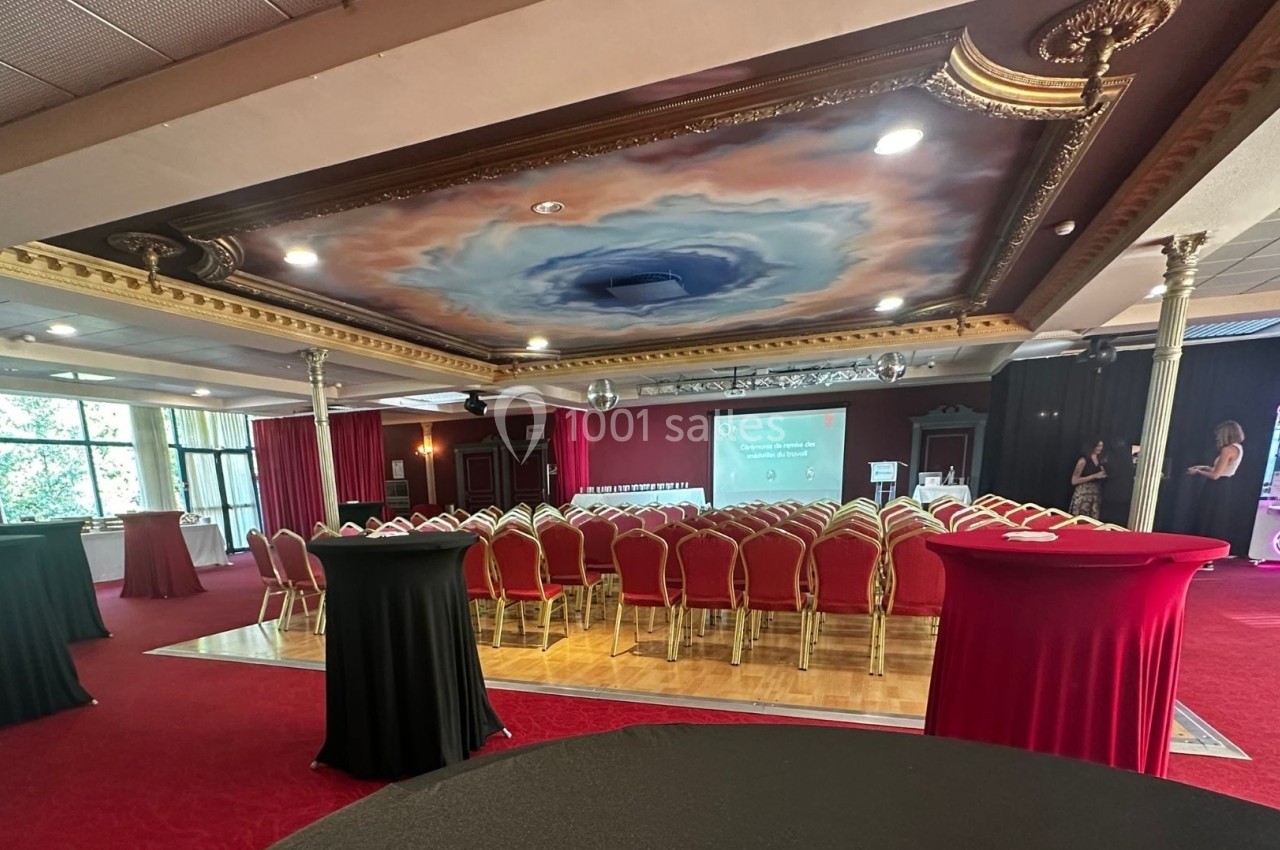 Salle adaptée pour conférence suivie d'un cocktail dinatoire Salle de réception avec plafond peint, chaises alignées face à un écran de projection, tables hautes en premier plan.