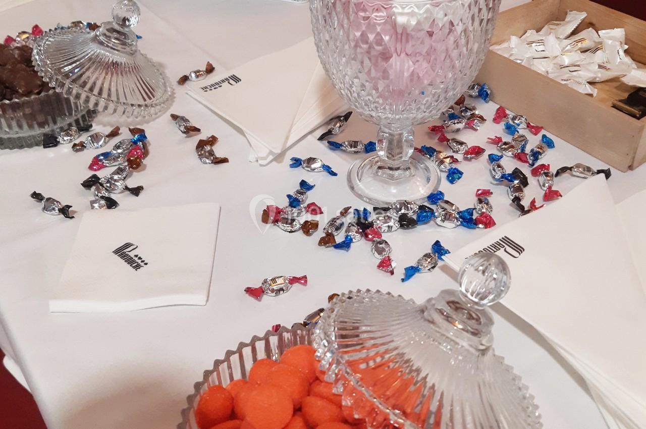 Bonbonnières en verre remplies de sucreries colorées sur une table blanche avec des serviettes et des bonbons dispersés.