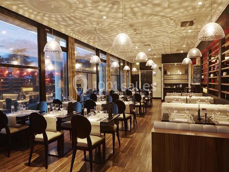 Salle de restaurant élégante avec tables dressées, grandes baies vitrées et éclairage suspendu diffusant une lumière…