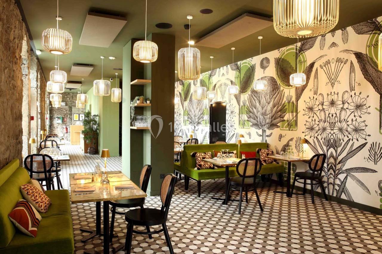 Salle de restaurant lumineuse avec décoration végétale, banquettes vertes, chaises noires et sol à motifs géométriques.