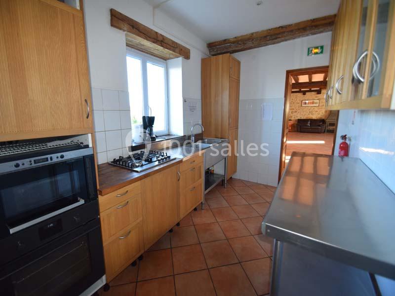 Cuisine équipée avec plan de travail en bois, évier inox, plaques de cuisson, four encastré et carrelage au sol.