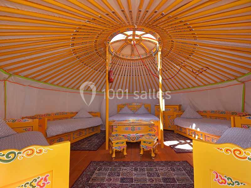 Intérieur d'une yourte colorée avec lits, mobilier en bois peint et tapis au sol.