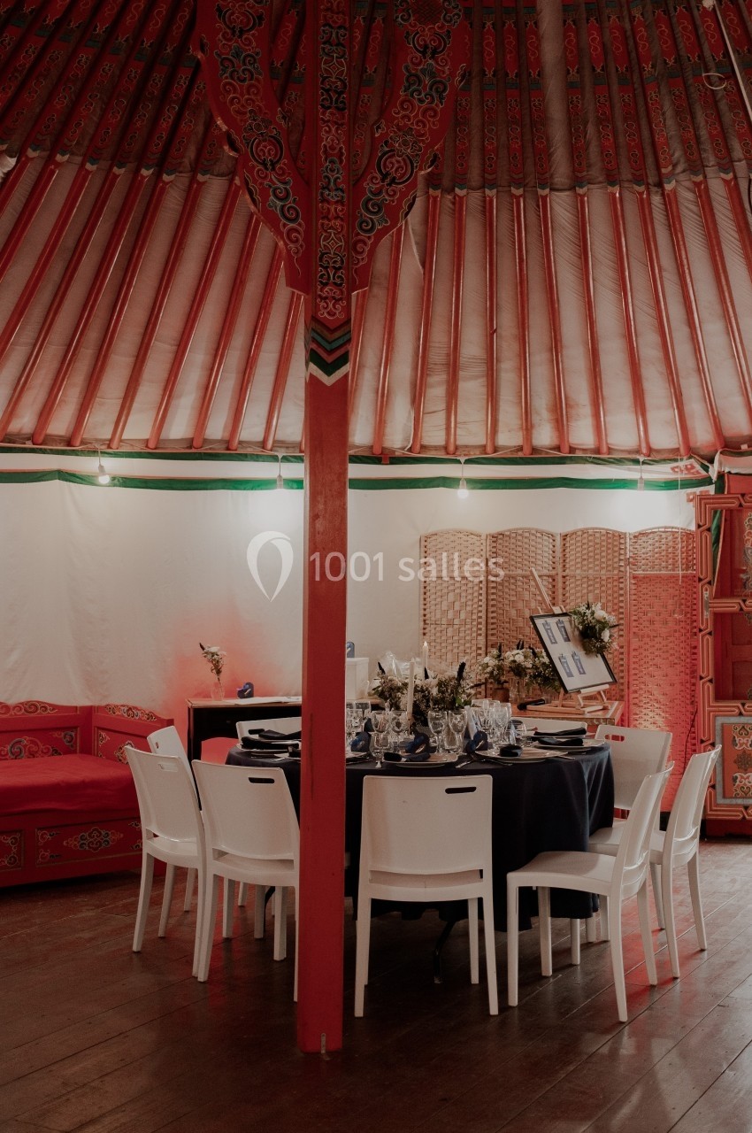 Salle décorée dans une yourte traditionnelle avec une table dressée, des chaises blanches et des éléments colorés.