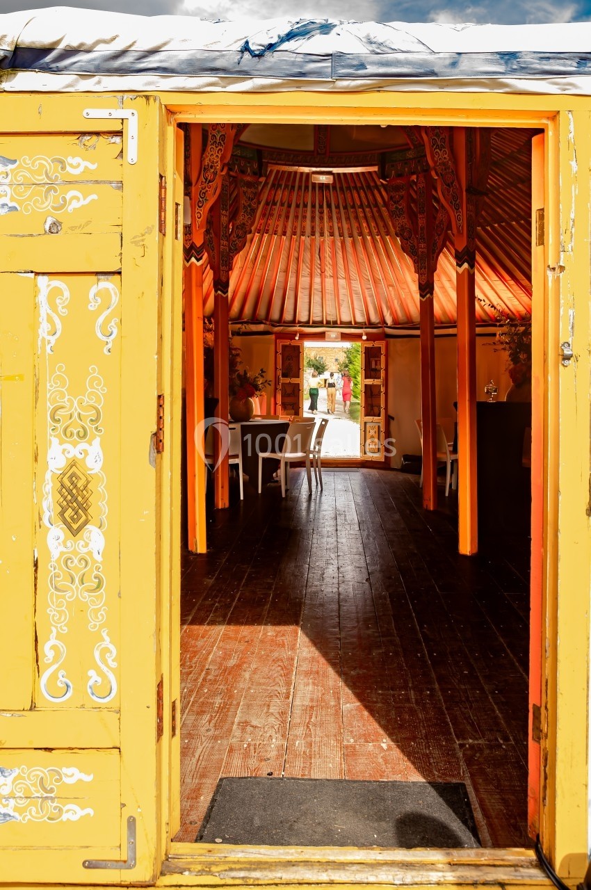 Vue intérieure d'une yourte colorée avec des motifs décoratifs, des tables blanches et une lumière naturelle.