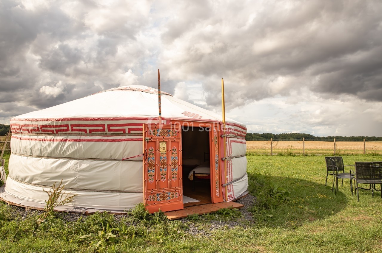 Yourte traditionnelle blanche avec porte décorée, installée dans un champ verdoyant sous un ciel nuageux.