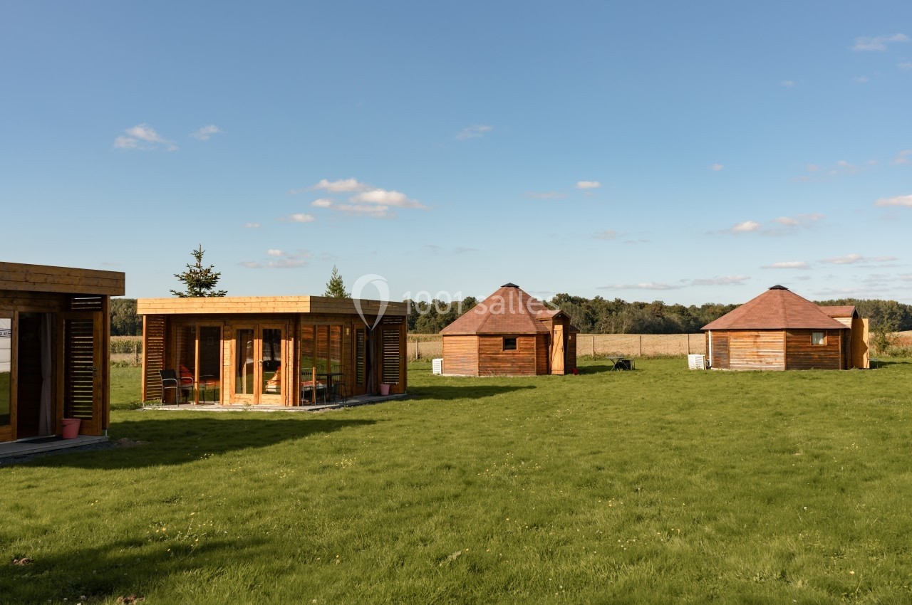 Chalets en bois modernes et petites cabanes sur un terrain herbeux sous un ciel dégagé.
