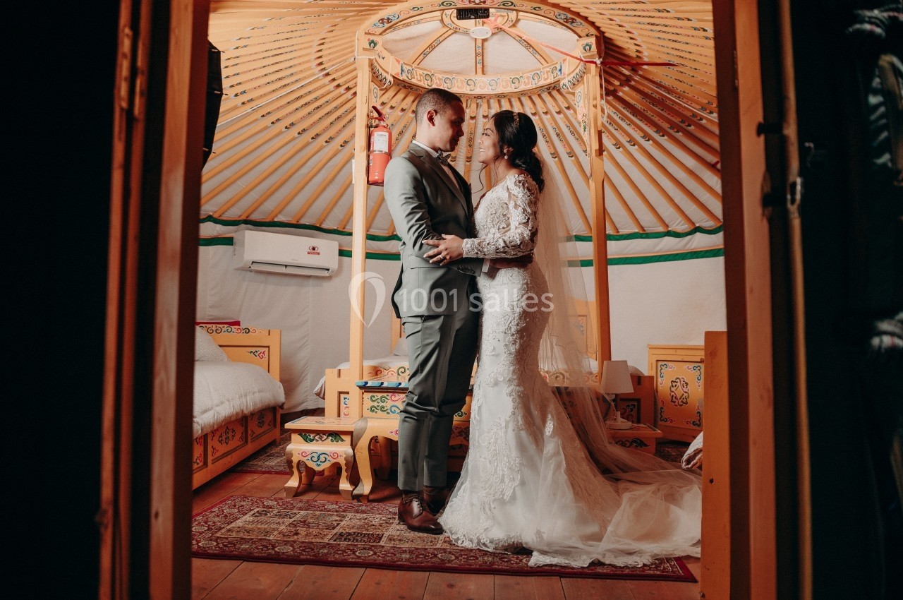 Un couple en tenue de mariage se tient debout dans une yourte décorée de motifs traditionnels.