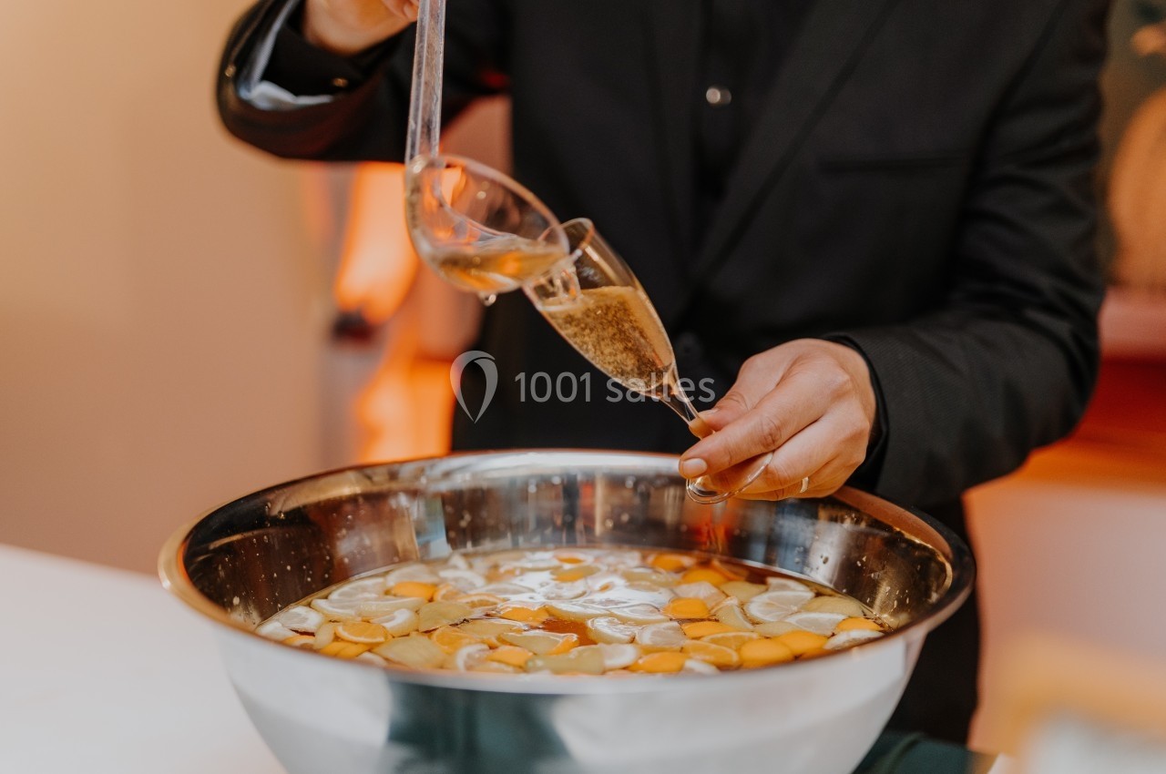 Une personne sert un verre de punch à l'aide d'une louche dans un grand bol contenant des morceaux de fruits.