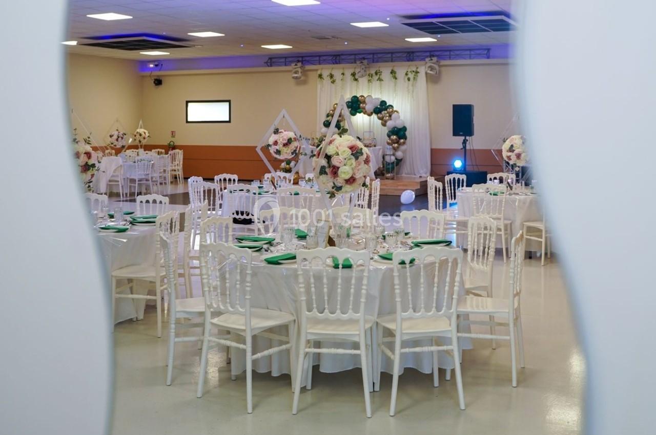 Salle de réception décorée avec des tables rondes, nappes blanches, chaises assorties et ornements floraux.