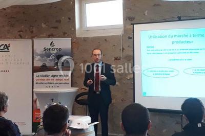 Lit double avec une couverture colorée, deux oreillers, tables de chevet en bois et une lampe dans une chambre simple.