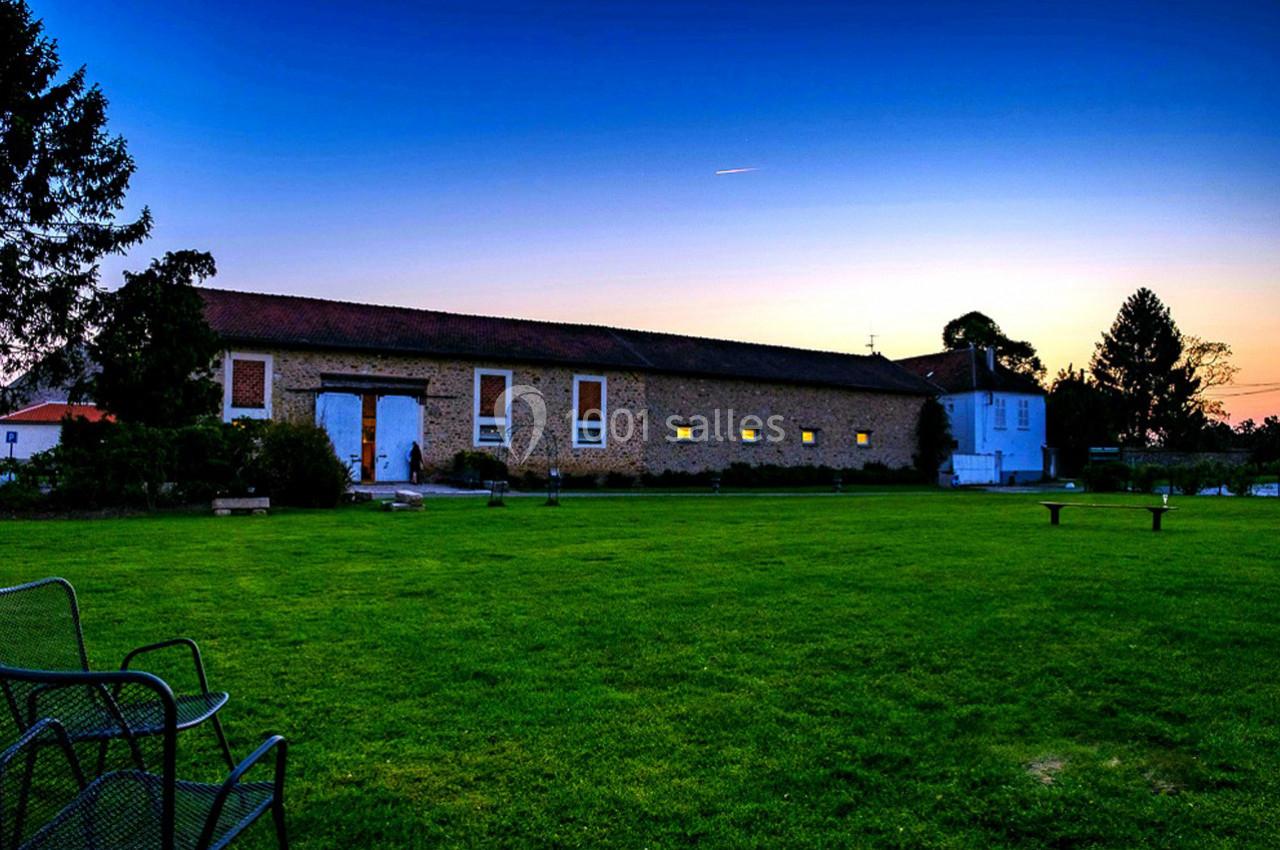 Bâtiment en pierre avec fenêtres éclairées, entouré d'une pelouse verte, au crépuscule sous un ciel dégagé.