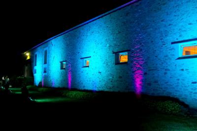 Lit double avec une couverture colorée, deux oreillers, tables de chevet en bois et une lampe dans une chambre simple.