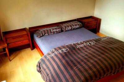 Lit double avec une couverture colorée, deux oreillers, tables de chevet en bois et une lampe dans une chambre simple.