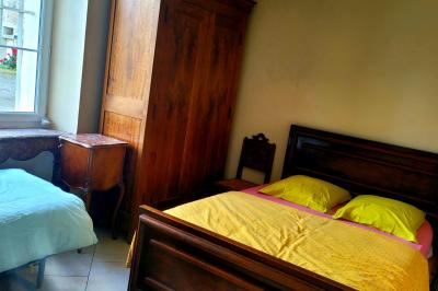 Lit double avec une couverture colorée, deux oreillers, tables de chevet en bois et une lampe dans une chambre simple.