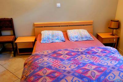 Lit double avec une couverture colorée, deux oreillers, tables de chevet en bois et une lampe dans une chambre simple.