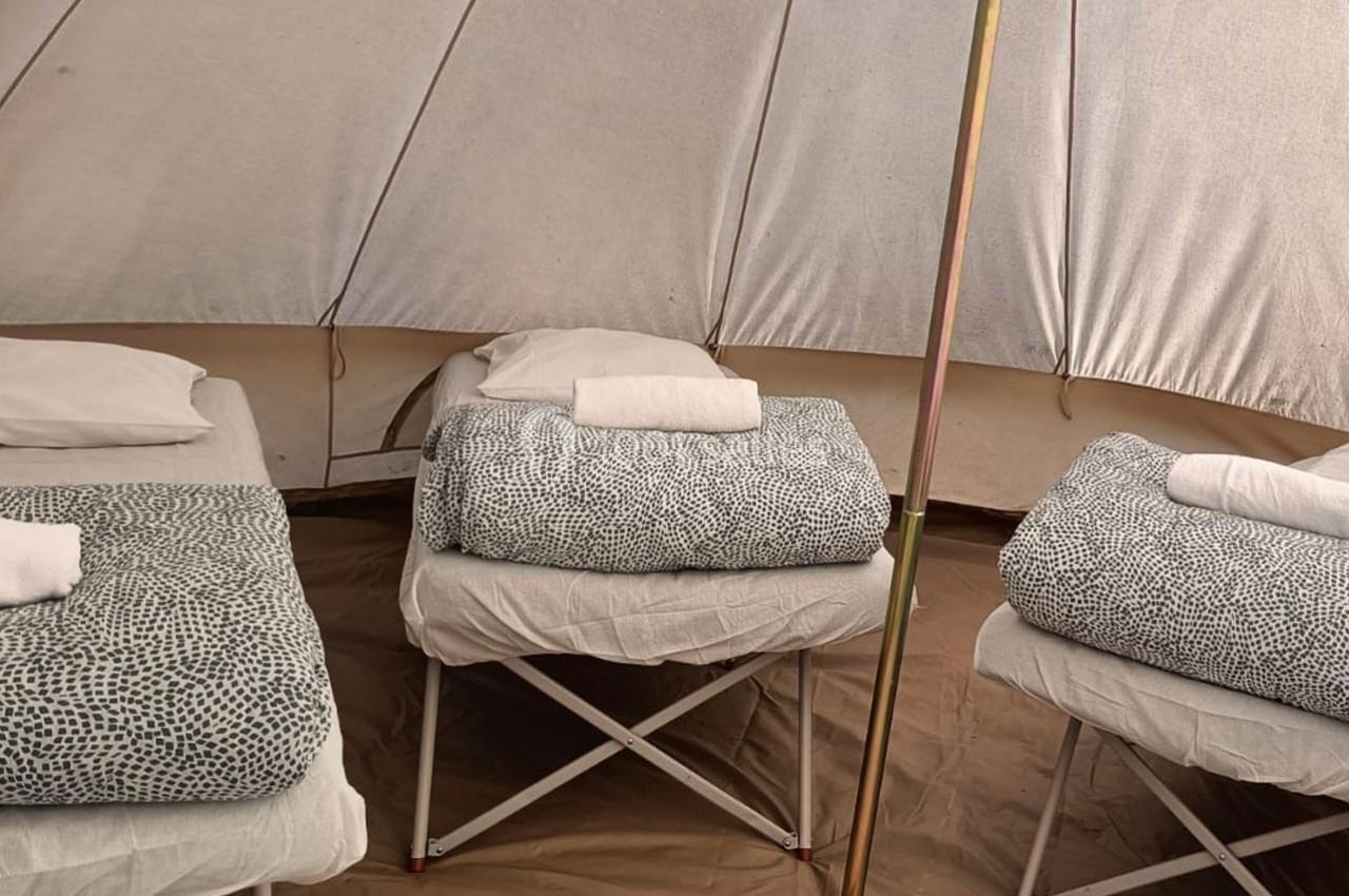 Trois lits simples avec draps à motifs et serviettes blanches dans une tente beige.