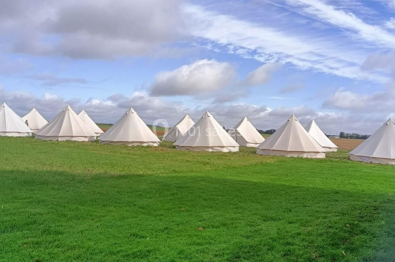 Tentes blanches en toile disposées sur une prairie verte sous un ciel partiellement nuageux.