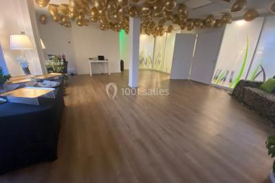 Salle lumineuse avec parquet, plafond décoré de ballons dorés, table avec plantes et vue sur des bâtiments urbains.