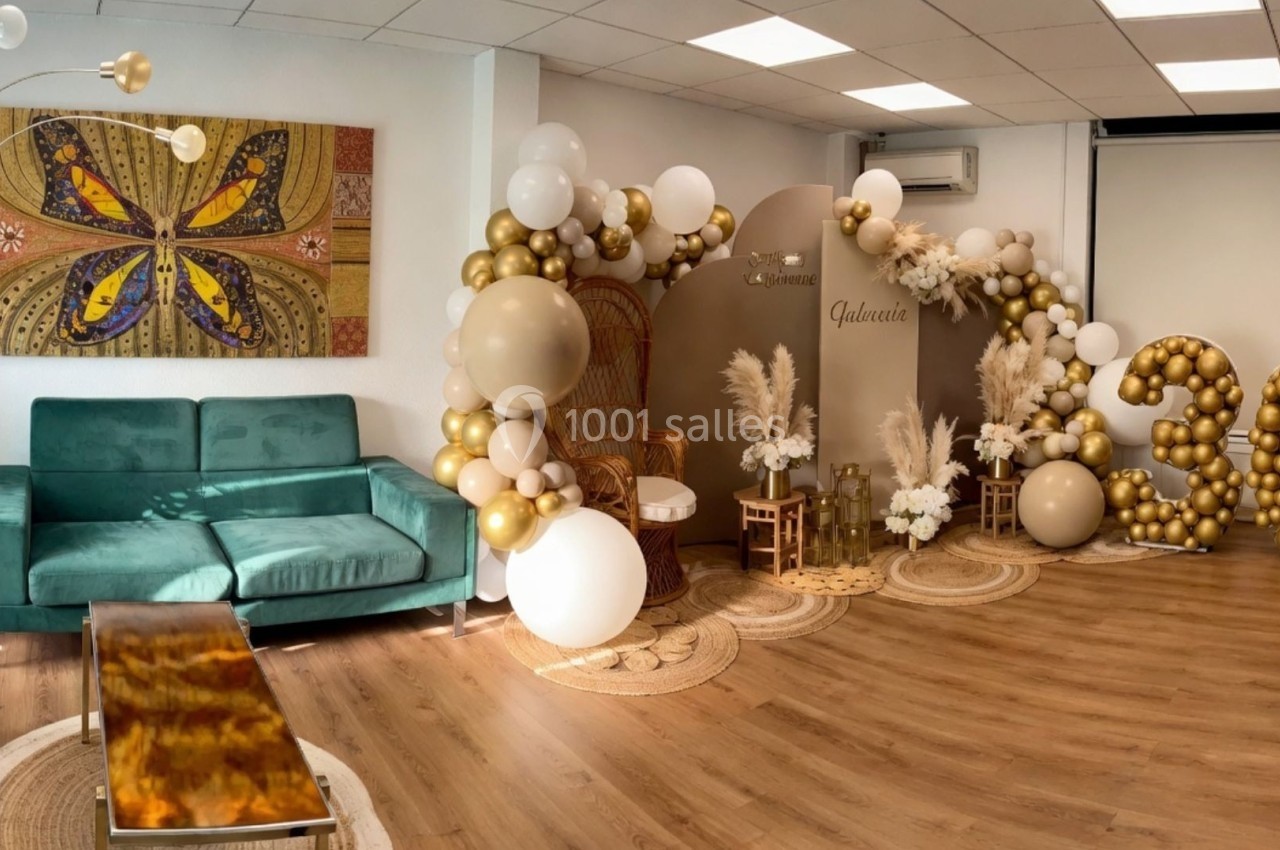 Salon décoré avec des ballons dorés et blancs, fauteuil en rotin, tapis en jute et tableau mural coloré.