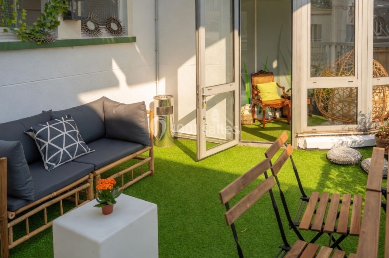 Terrasse avec mobilier en bois, canapé, table, chaises, plantes et sol en gazon synthétique, éclairée par le soleil.