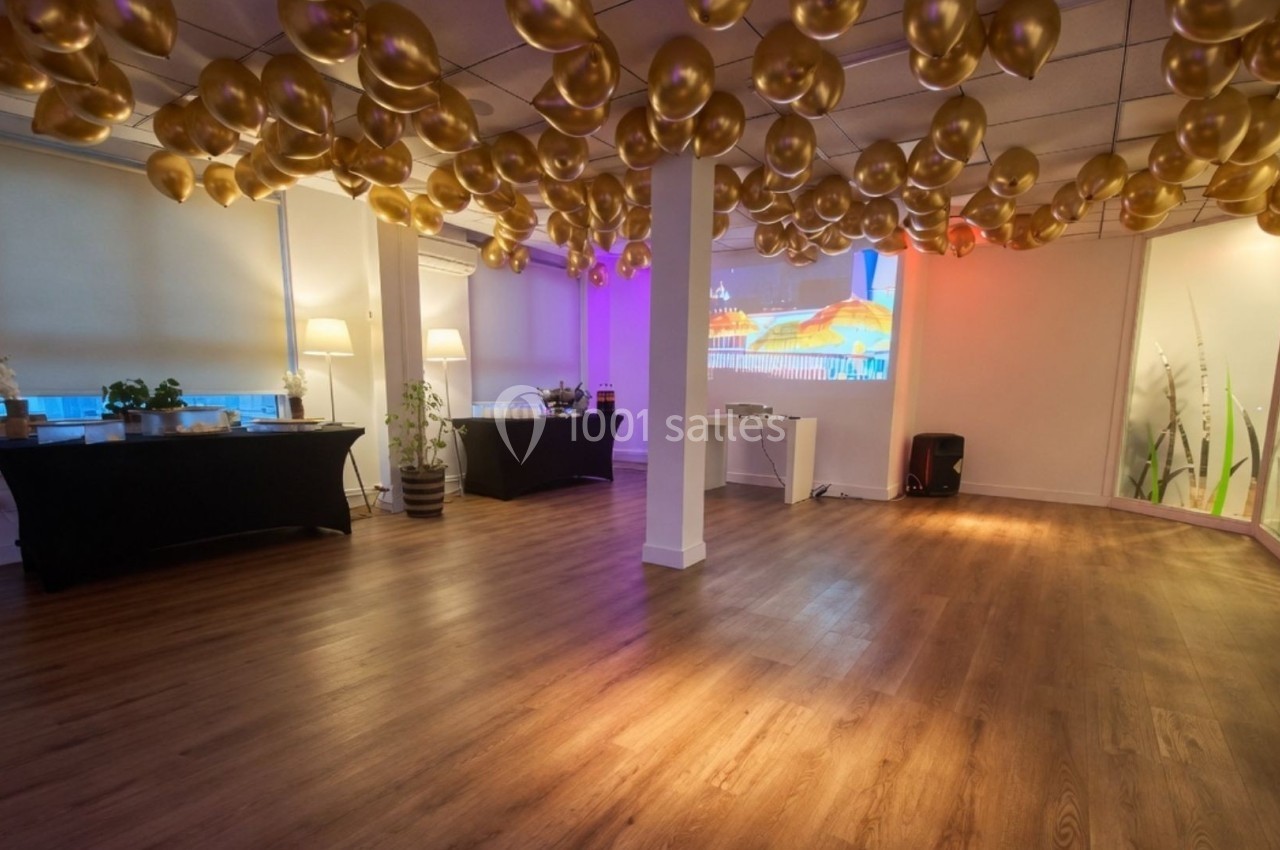 Salle de réception avec parquet, ballons dorés suspendus, tables décorées et projection murale en arrière-plan.